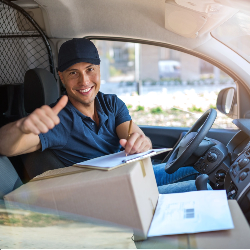 Friendly delivery driver smiling while holding clipboard inside van.